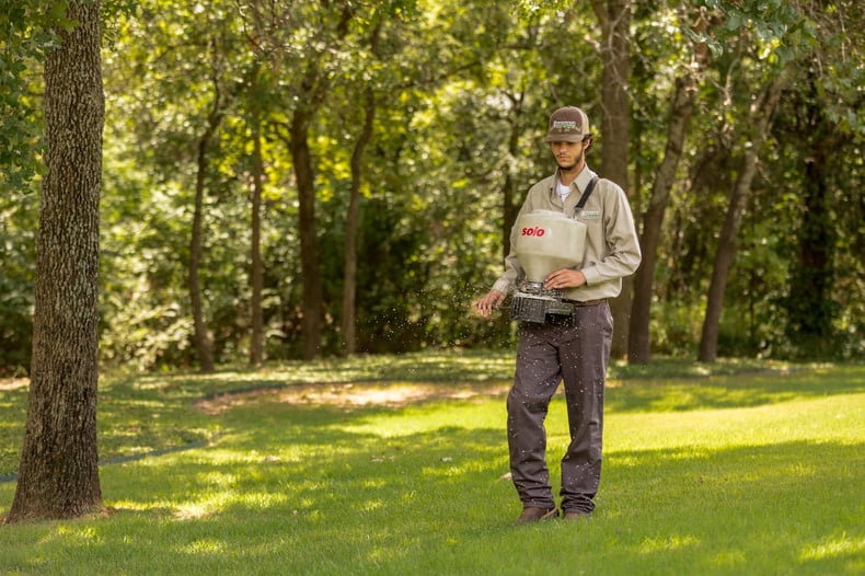 lawn care technician spreading fertilizer on Texas lawn