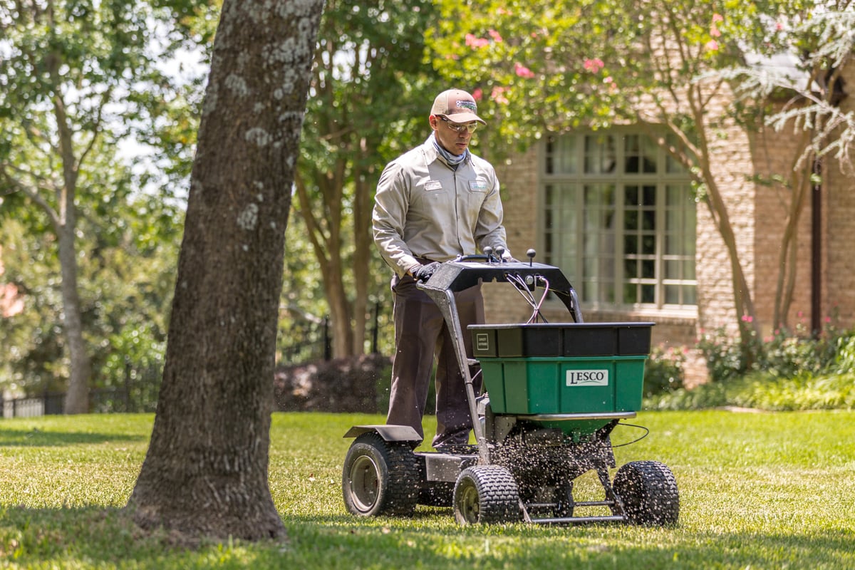 lawn technician uses ride on machine to spread fertilizer