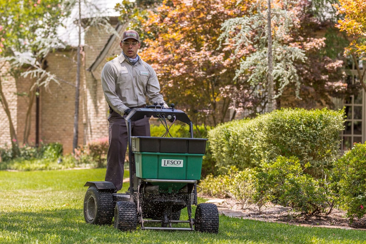 lawn technician spreads fertilizer with ride on machine