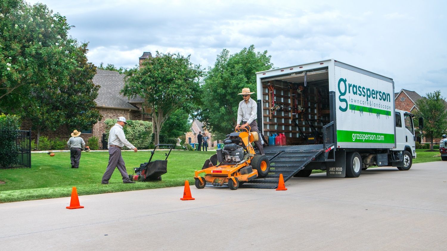 Grassperson lawn care and landscaping truck and crew members performing lawn maintenance
