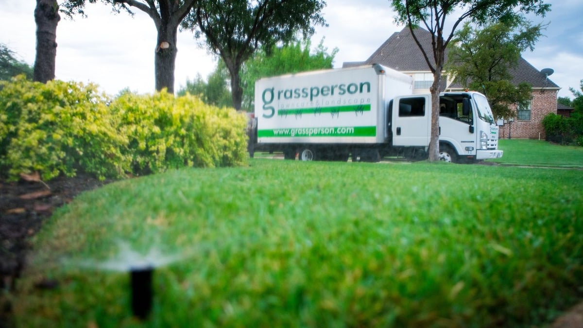 sprinkler head watering grass with grassperson truck parked on street