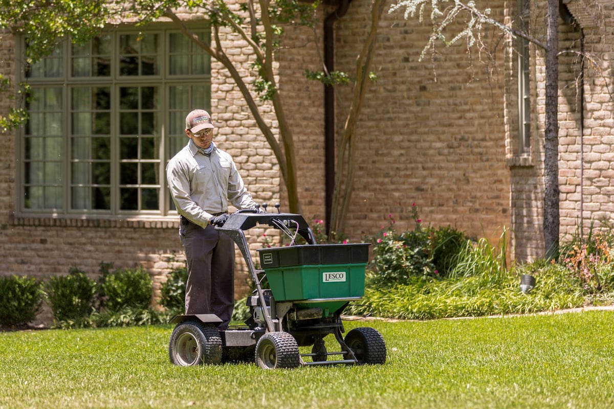 lawn technician uses ride on spreader to fertilize lawn