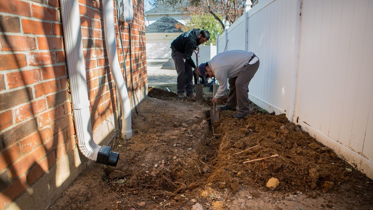 landscaping team installs drainage system near fence
