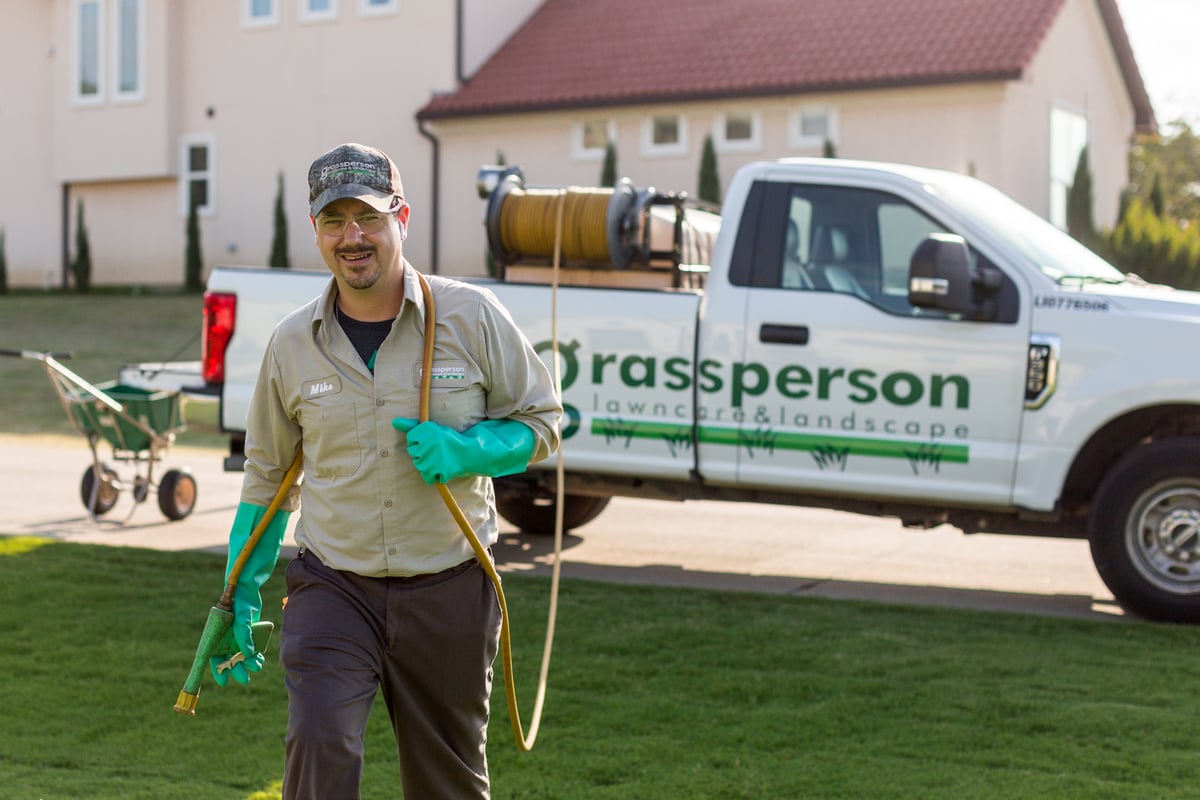 lawn care technician pulls hose to treat grass