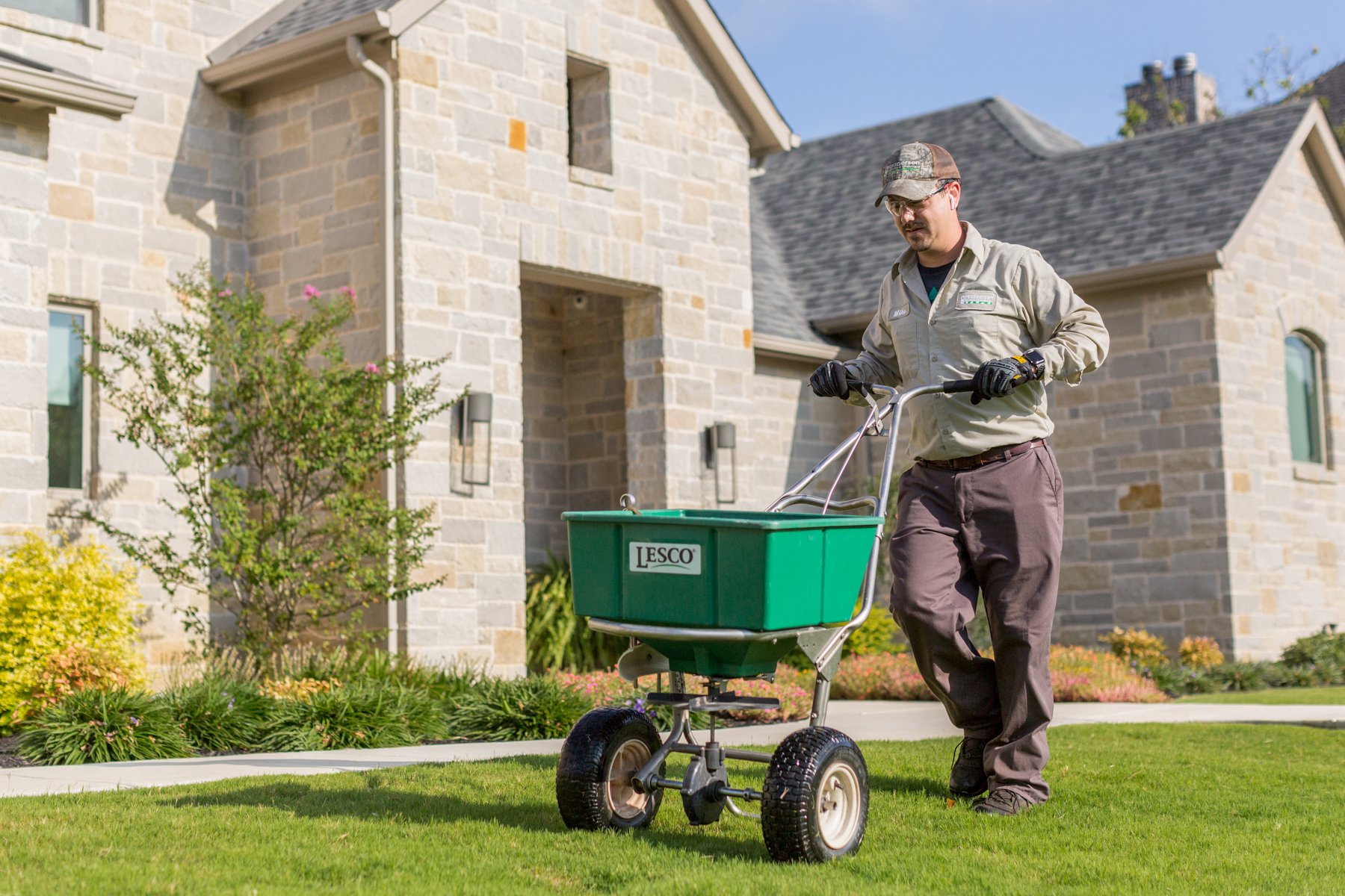 lawn care technician spreads granular fertilizer 