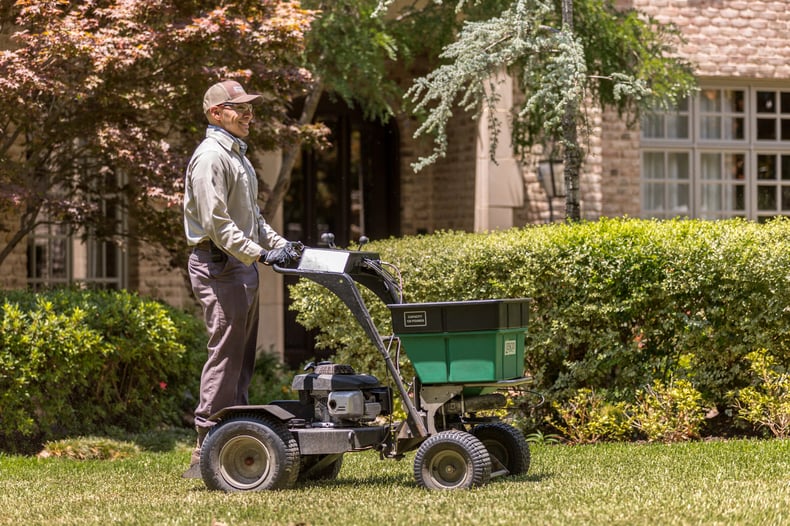 lawn technician spreads fertilizer with ride on machine